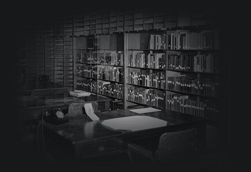 A room with desk and chairs and cataloged books shelved on bookcases around the room. 