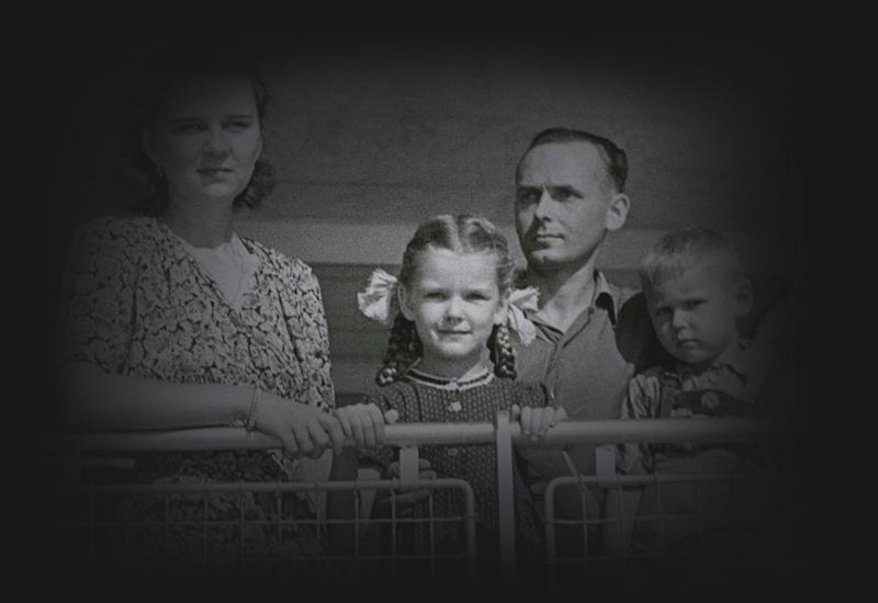 Maira Kalnins, wearing pigtails, standing at the ship's rail with her family. 