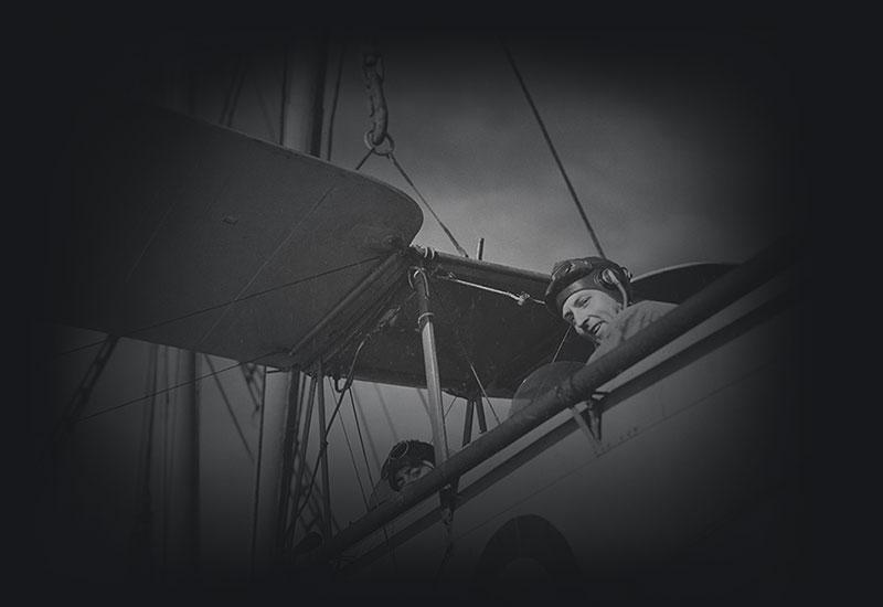 2 men looking down from the open cockpits of a biplane.