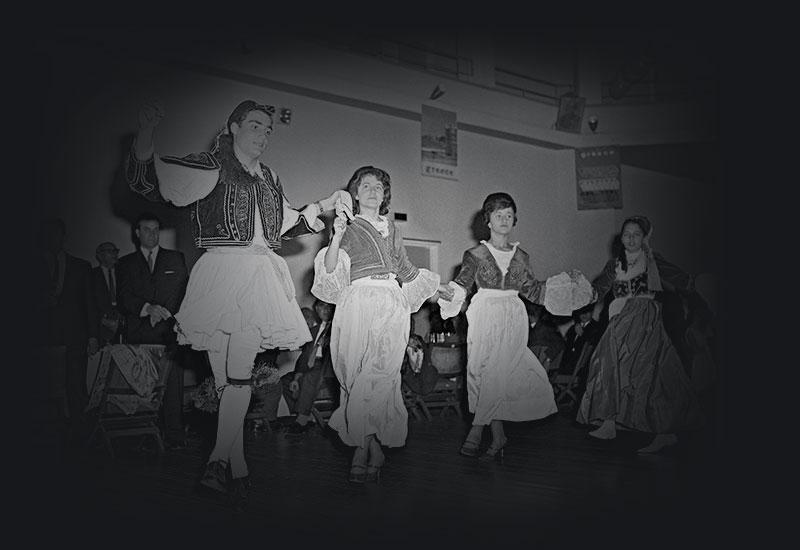 A man and 3 women in national costume dancing while holding hands.