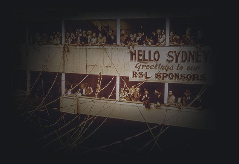 A ship with streamers from ship to wharf with people on deck holding a banner 'Hello Sydney! Greetings to our RSL sponsors'