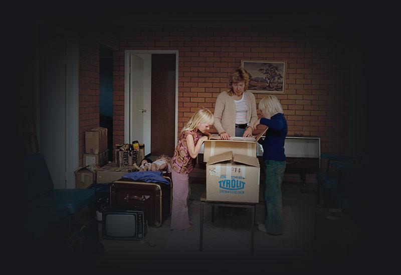 A woman and 2 children unpacking a box in a living room.