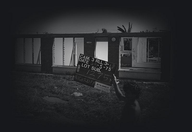 A man holding a housing allotment number sign infront of a damaged home.