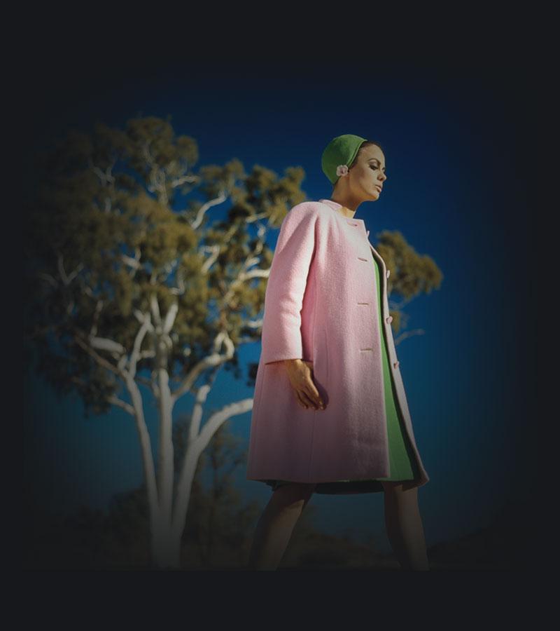 A woman modelling a pink coat over green dress near a large Ghost gum.