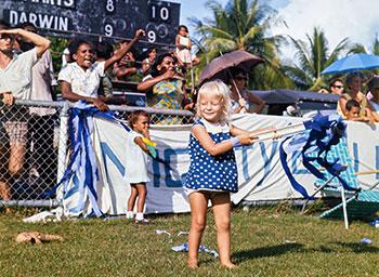 A young girl holds blue streamers while people cheer their football team.