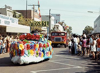 People line a street to see a colourful parade float carrying Miss RSL.