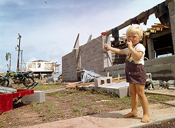 A boy with a red kite, a green trailbike and 2 destroyed buildings.