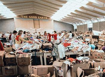 People sort clothes amongst piles of boxes inside a hall.