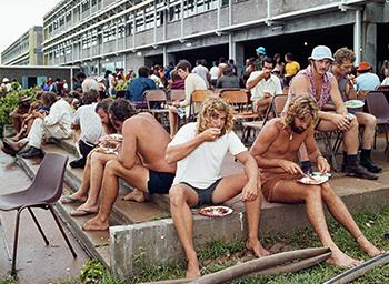 People sitting outside eating from paper plates.