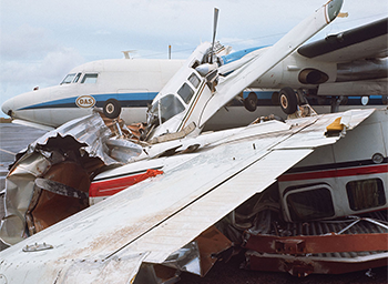 2 wrecked light aircraft positioned against a larger twin propeller aircraft.