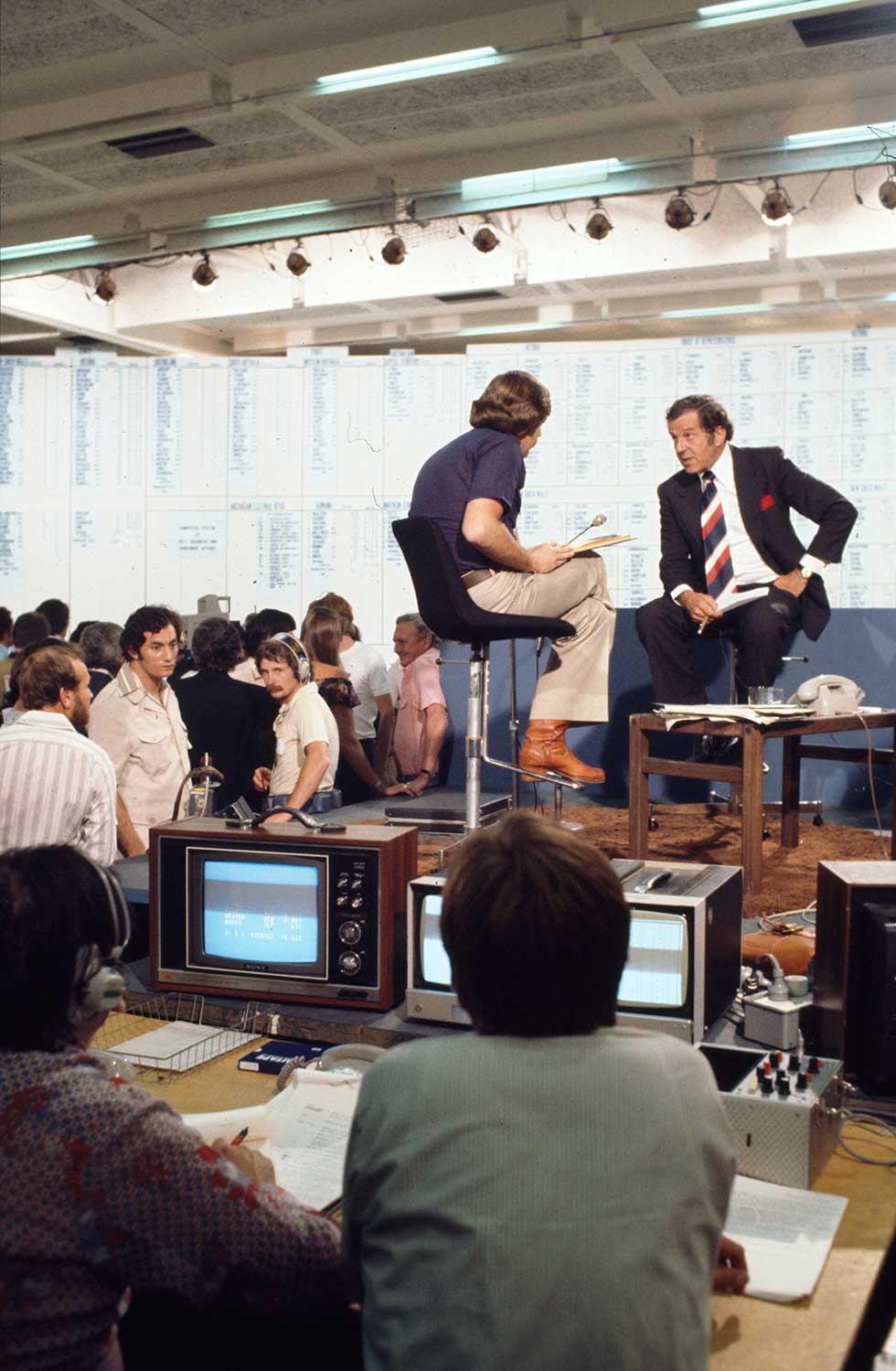 Don Chipp being interviewed by a television journalist on a platform surrounded by people in the National Tally Room.