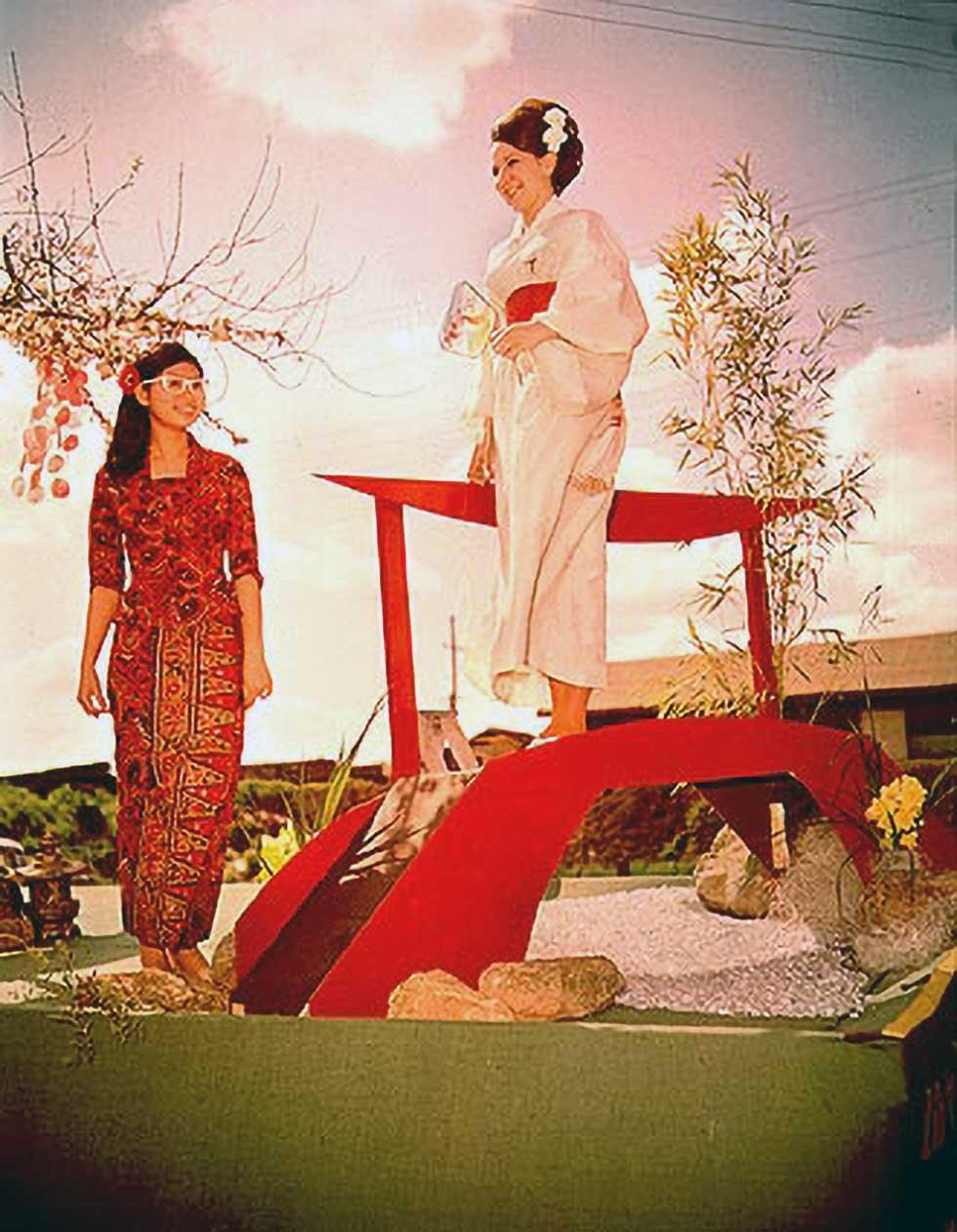 Two women standing in a staged Japanese garden wearing traditional style clothing.