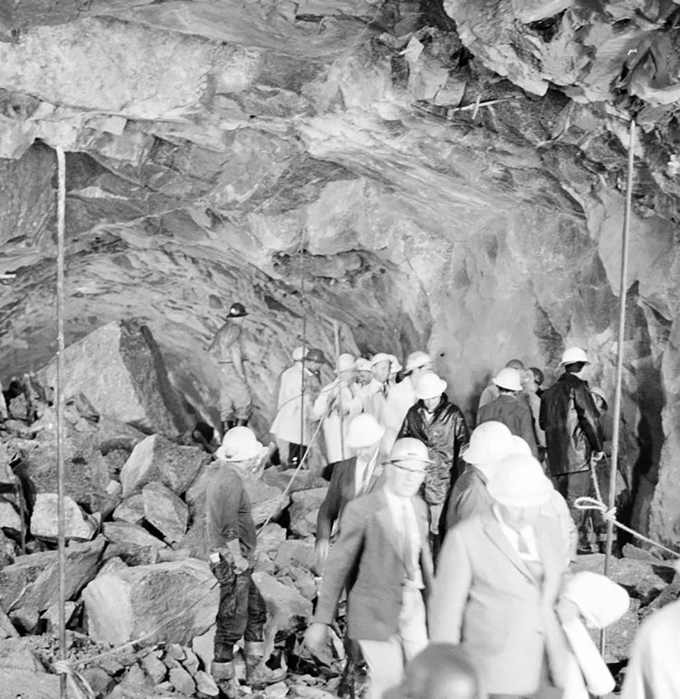 Miners and official guests picking their way through broken rocks.