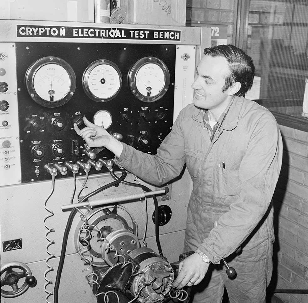 A man in overalls operating an electrical test bench.