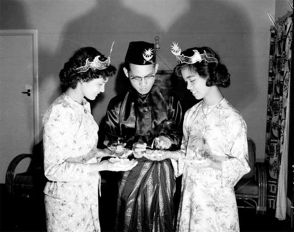 Three young Malayan students in traditional costume lighting candles.