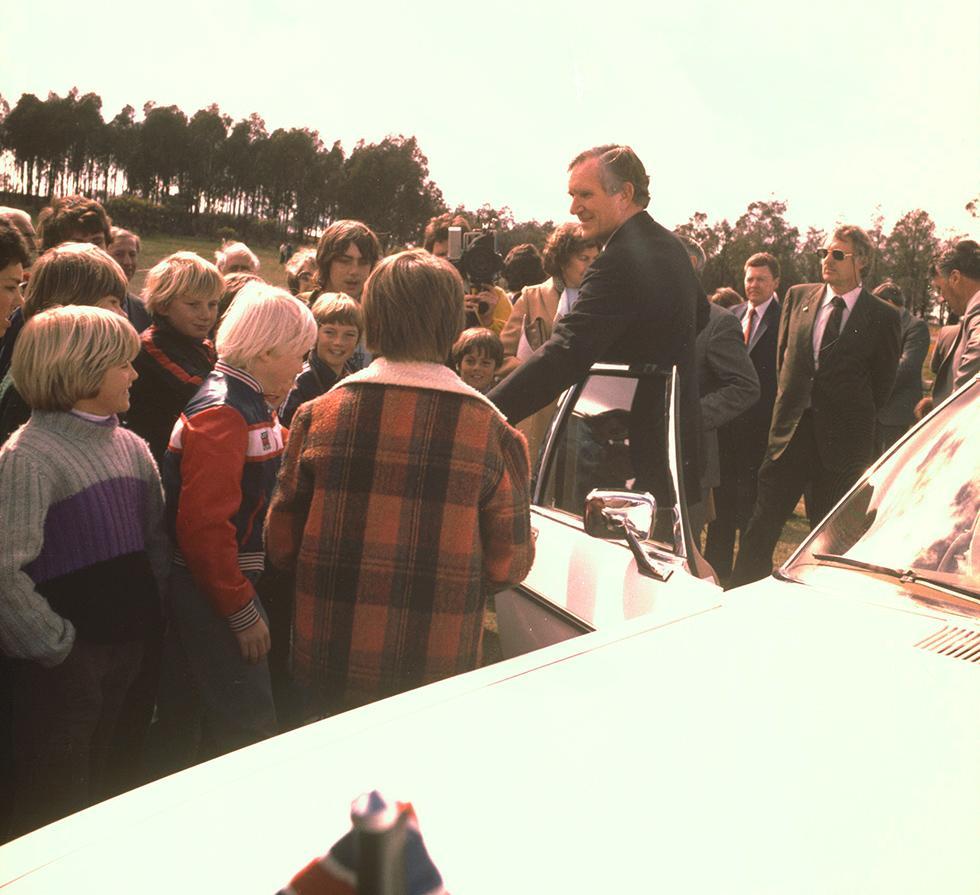 Malcolm Fraser standing beside his government car surrounded by a group of children. 