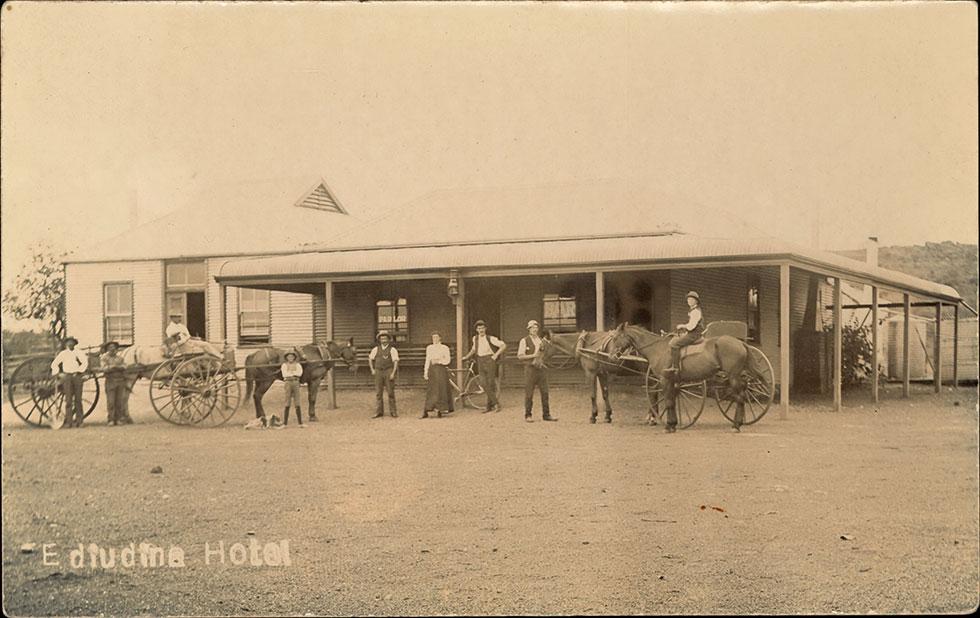 People and horses with carts gathered for a photo in front of a building.