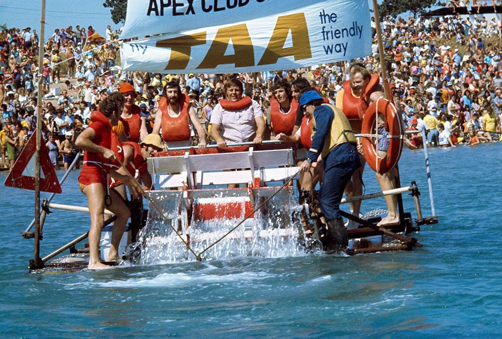 A human powered paddle boat with sponsors banner 'Apex Club' and 'Fly TAA the friendly way'.