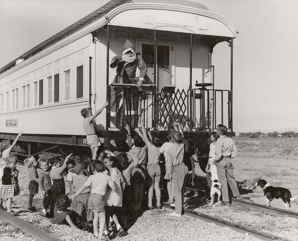 Young children and 2 dogs look up at Santa on a train.