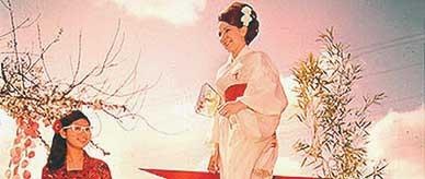 Two women standing in a staged Japanese garden wearing traditional style clothing.