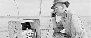 George Alder in a flat, dry and dusty paddock kneeling beside the first portable radio telephone in the outback.