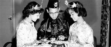 Three young Malayan students in traditional costume lighting candles.