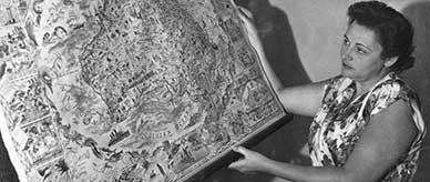 Nancy Wake holding a large tapestry depicting an illustrated map of Australia.