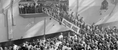 Troops returned from Vietnam disembarking from a ship displaying banner ‘Welcome home’.