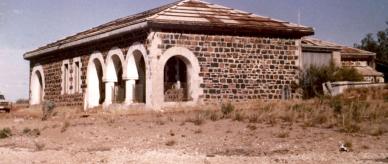 An abandoned grey stone building with arches supported on columns.