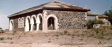 Abandoned grey stone building with arches supported on columns.