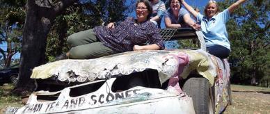 4 women sitting on a car painted with 'More than tea and scones.'