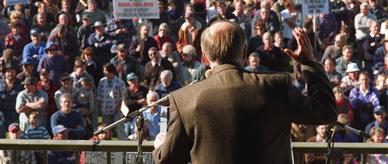 John Howard addressing a crowd with the outline of a bulletproof vest beneath his jacket.