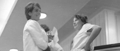 2 women standing at a bar, one with a beer in her hand. 