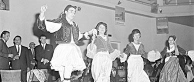 A man and 3 women in national costume dancing while holding hands.