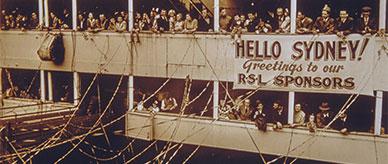 A ship with streamers from ship to wharf with people on deck holding a banner 'Hello Sydney! Greetings to our RSL sponsors'