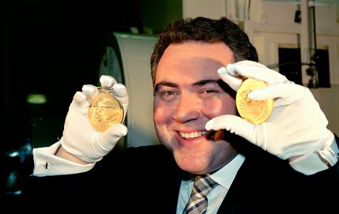 Joe Hockey wearing white gloves and holding two Sydney Olympic gold medals at the Australia Mint