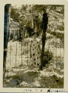 Iseko Williams standing under a tall tree fern wearing a light coloured dress and white shoes.