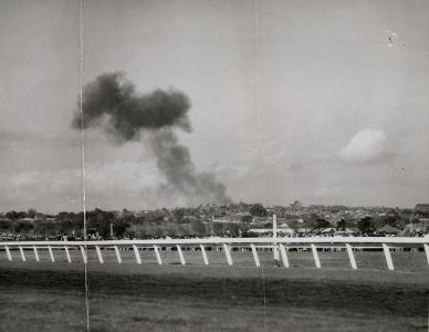 A plume of black smoke rising from north Melbourne viewed from across Flemington Racecourse.