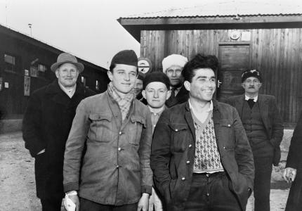 A group of 7 men at a displaced persons camp smiling at the camera.