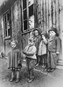 A group of children standing outside a battered building, looking distrustfully at the camera.