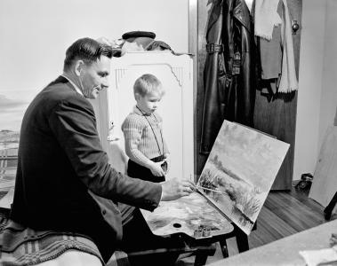 Otto working on a landscape painting on a desk easel, watched by his son.