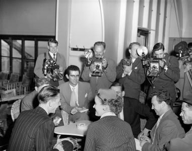 Barbara and Dennis Porritt facing away from the camera, being interviewed and photographed by the press. 