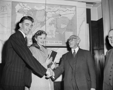 Dennis Porritt shakes hand with the Chairman of the State Electricity Board, with Barbara smiling in the background. 