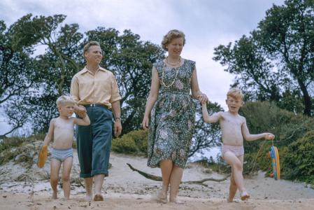 A mother and father with two sons in speedos walking down a sand dune at a beach.