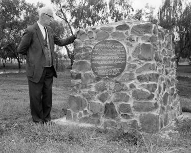 A man in a suit standing next to a stone monument.