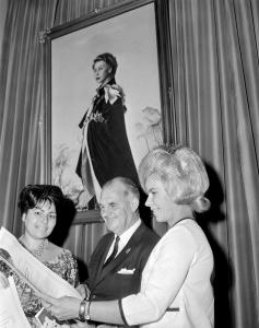 Immigration Minister Sir Hubert Opperman with two new Australian citizens standing in front of a portrait of the Queen. 