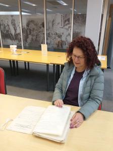 A woman seated at a table viewing an open document.