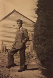 Tony dressed in a suit, standing near a timber building.