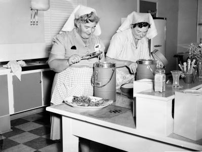 2 women placing prepared meals into canisters for delivery to Meals on Wheels pensioners.