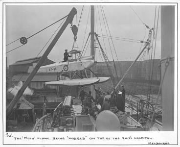 Biplane being hoisted onto a ship.